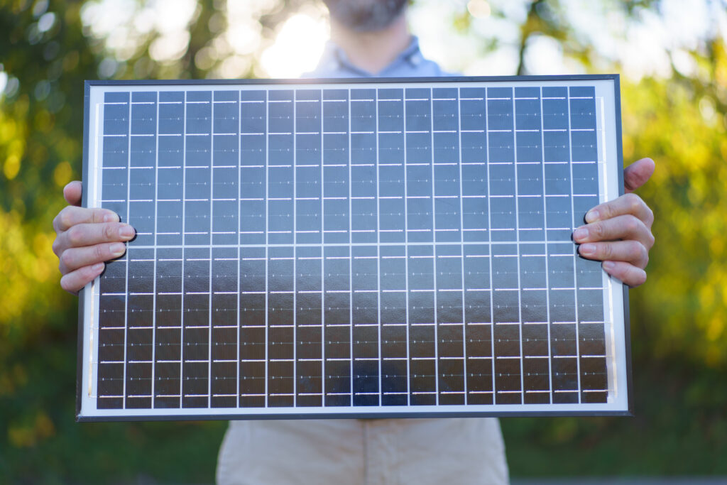 Close-up of businessman holding solar panel, standing outdoor at garden.