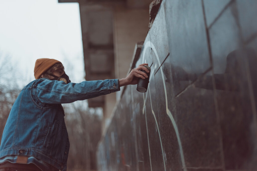 man in respirator painting graffiti on building with can